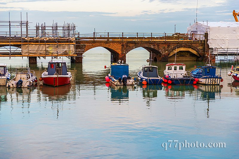 Boats and ships moored in a small port, in the background stone 